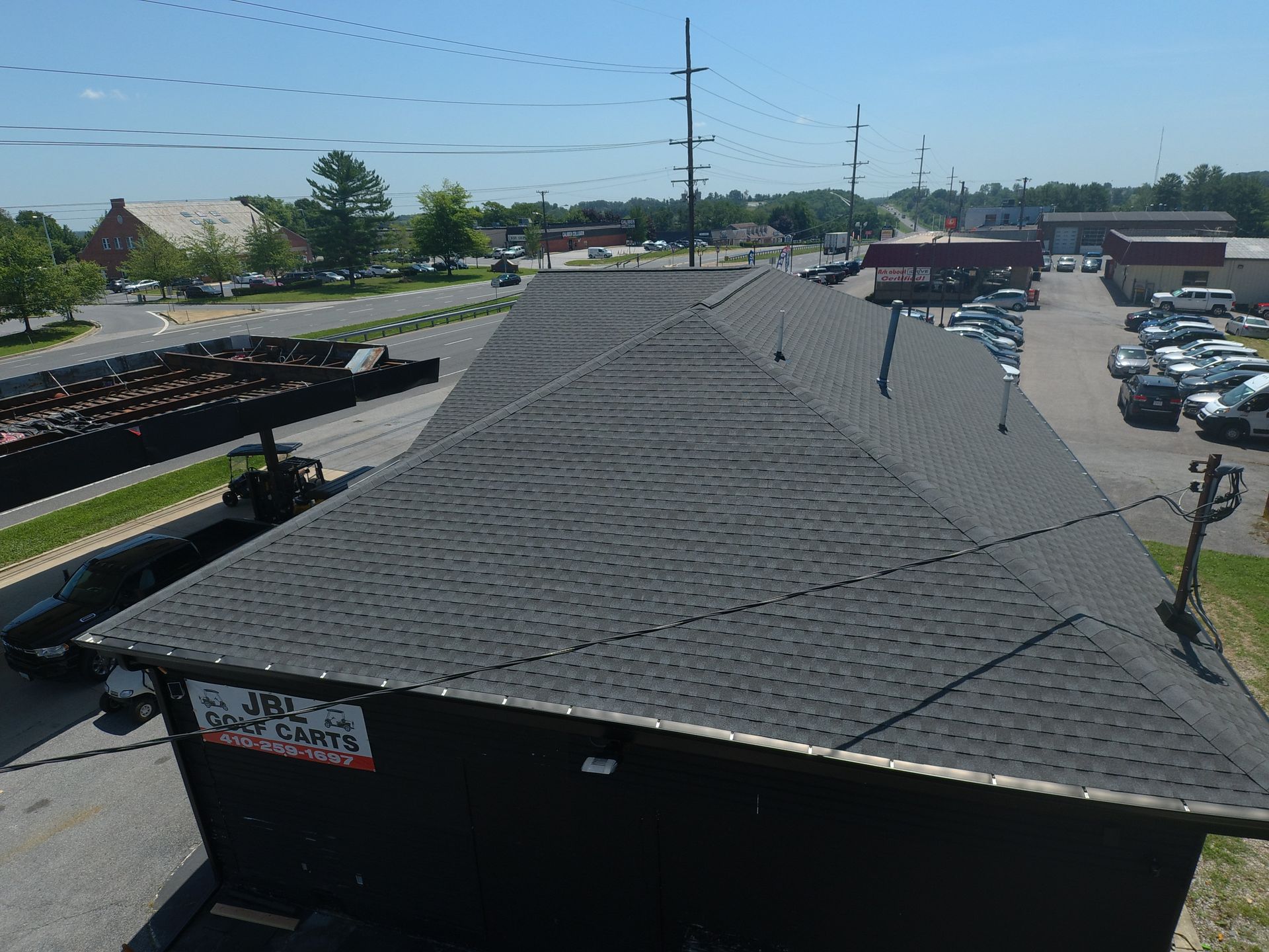Row of dark shingled buildings in a parking lot under a clear blue sky, with cars and power lines nearby