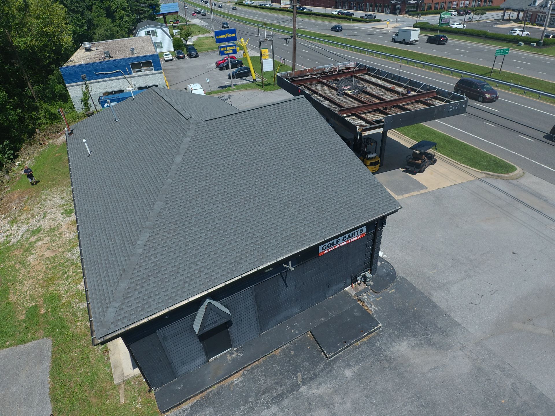 Aerial view of a black-roofed commercial building beside a road and parking lot