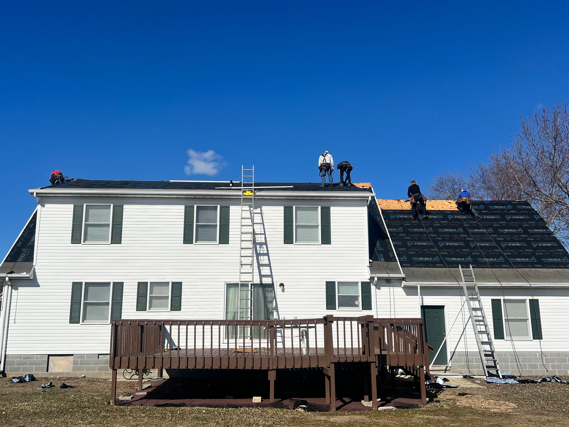 Two-story house with workers repairing the roof and a ladder against the front deck