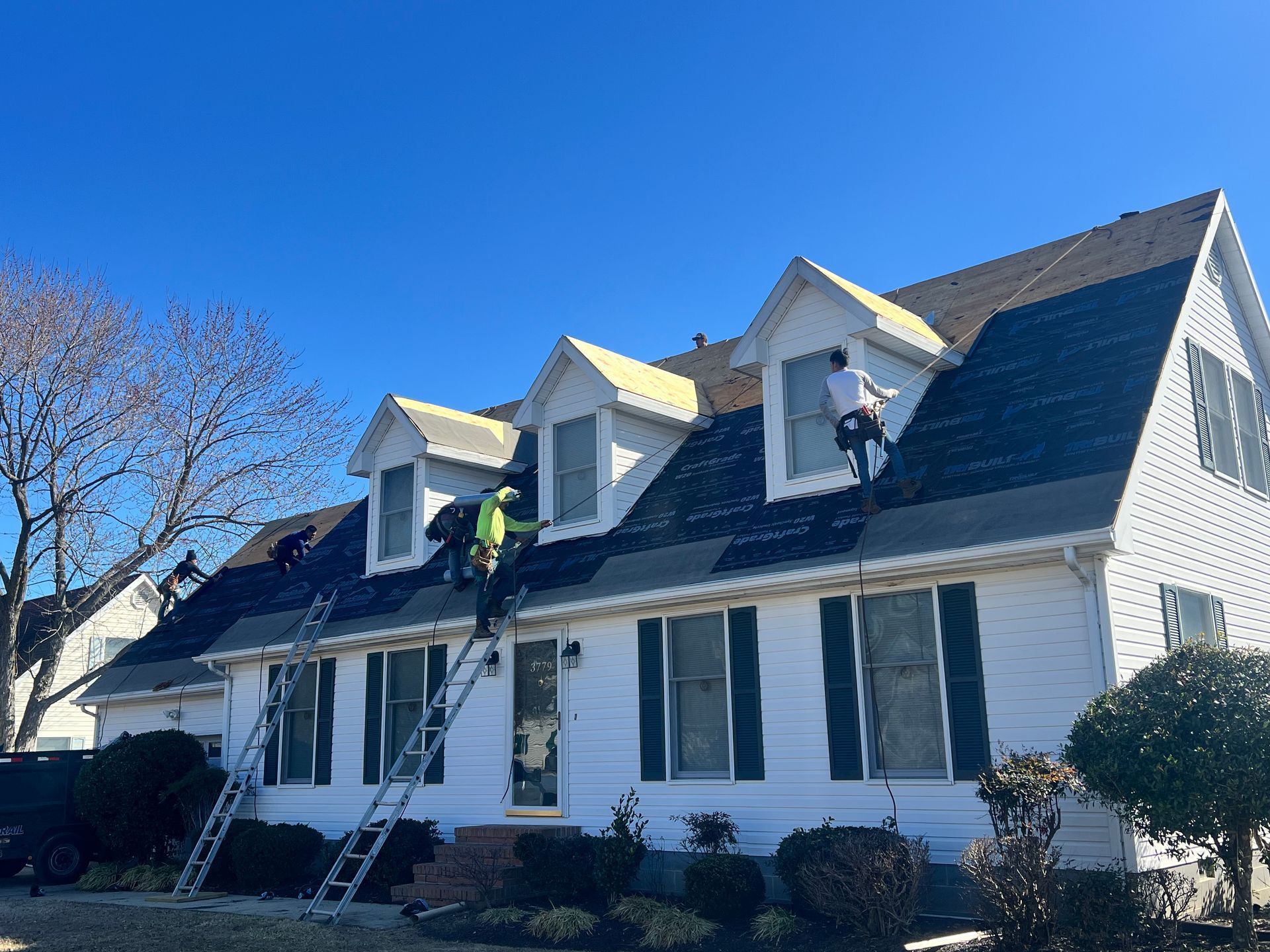 Workers on a roof repairing a white house with dark shingles on a clear day