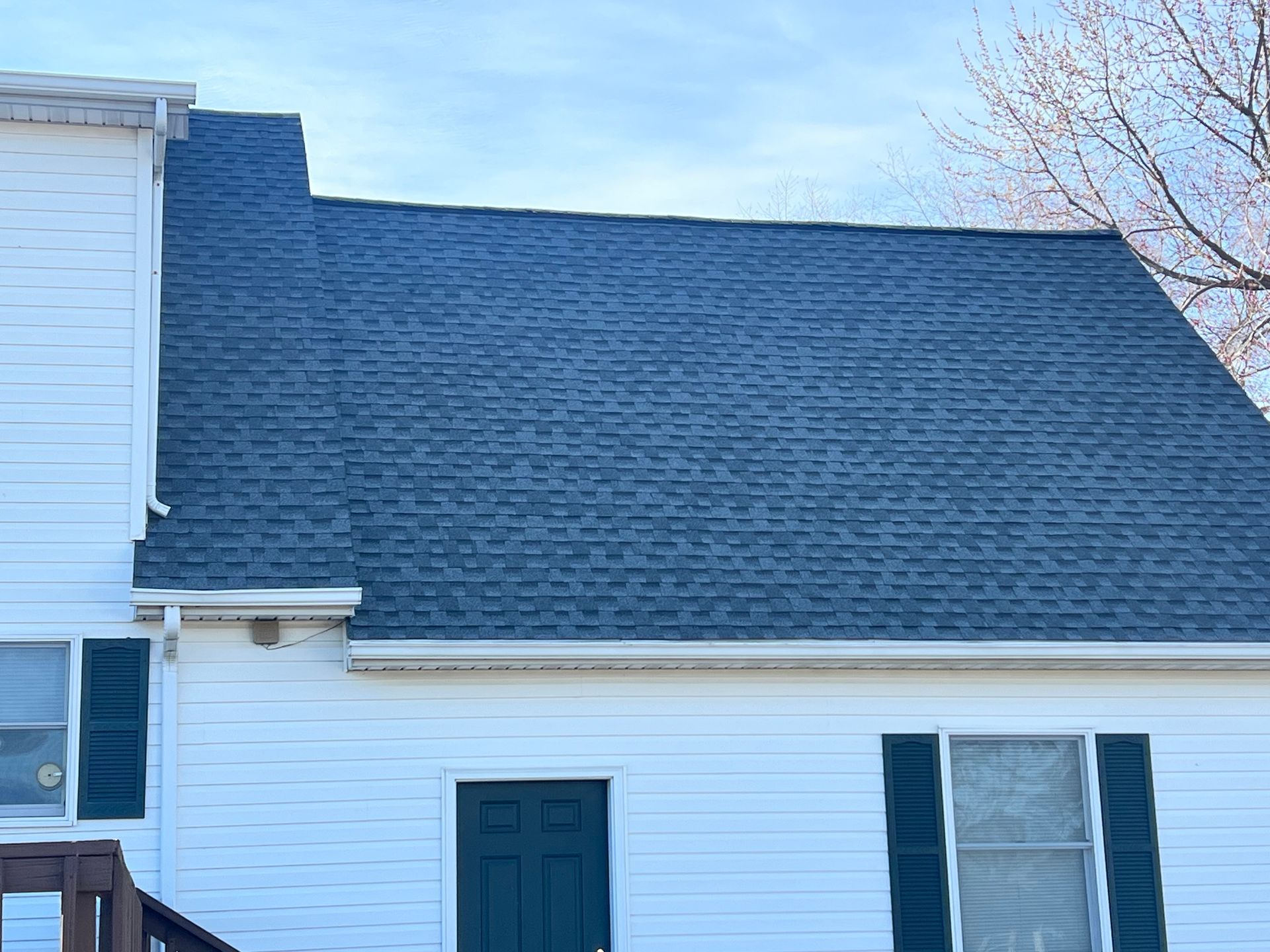 White house exterior with blue shingled roof, teal door, and blue shutters under a clear sky