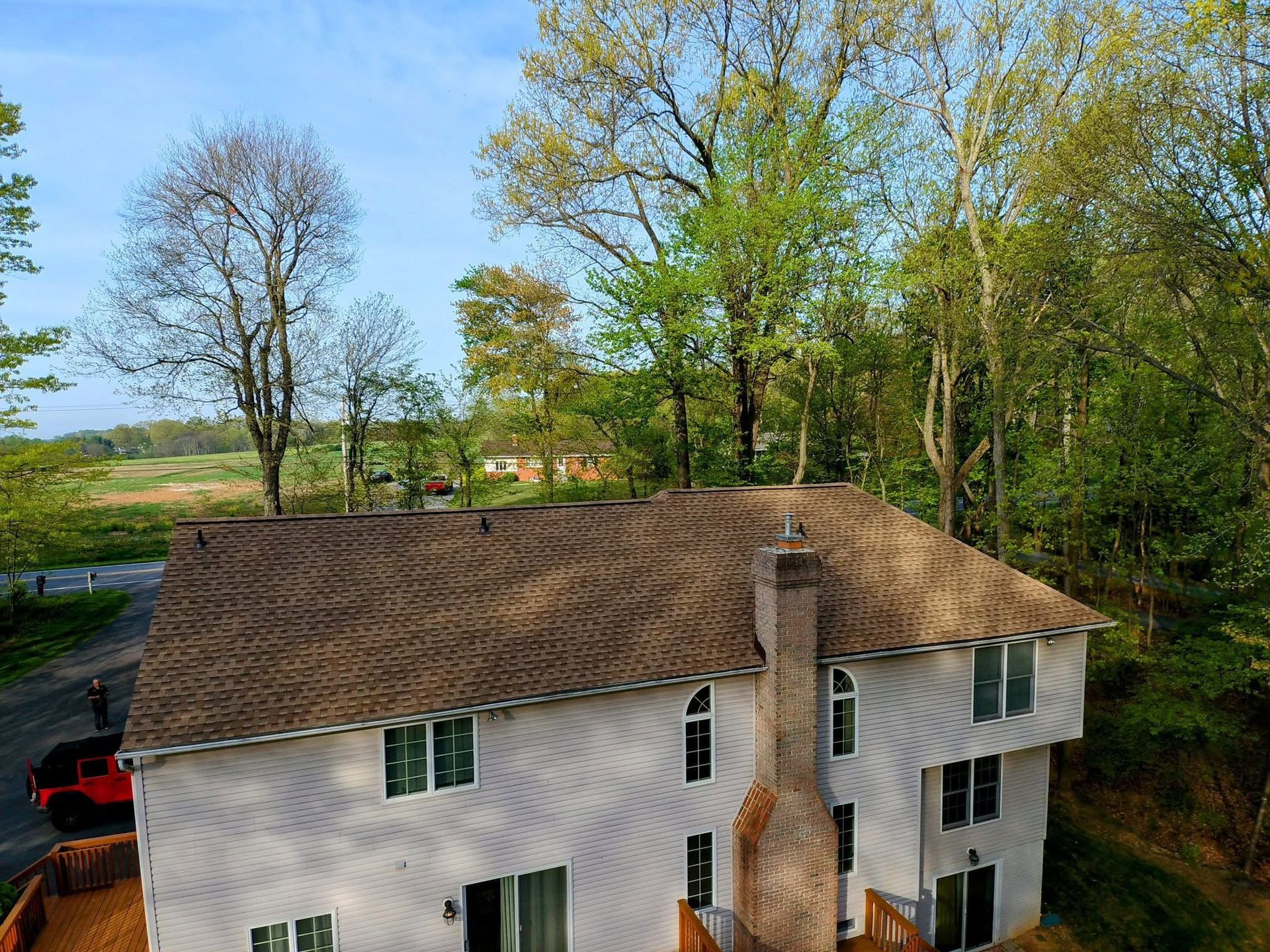 White house with brown roof beside trees and a road on a sunny day