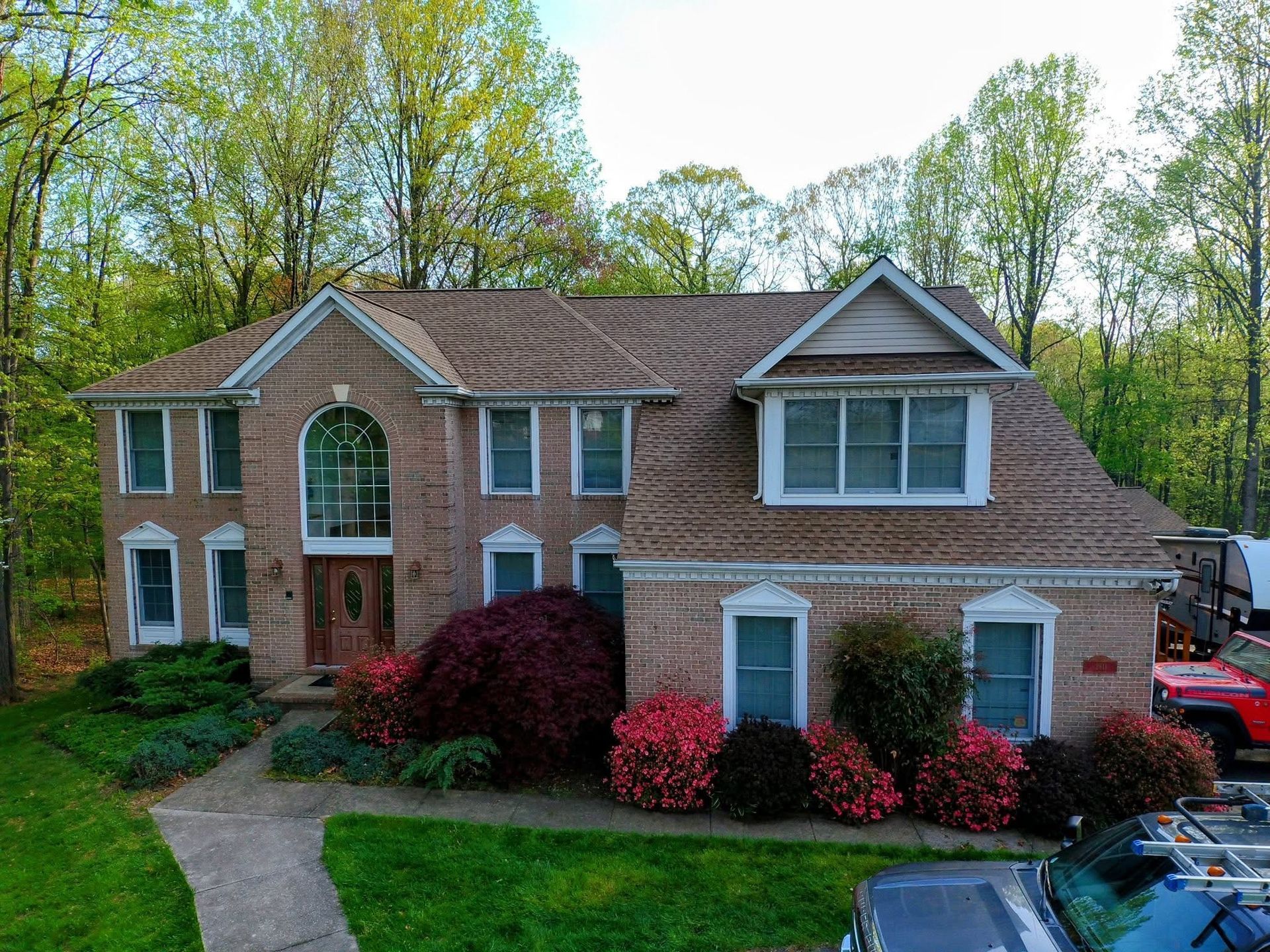 Two-story brick suburban house with a front lawn, arched entry, and blooming shrubs