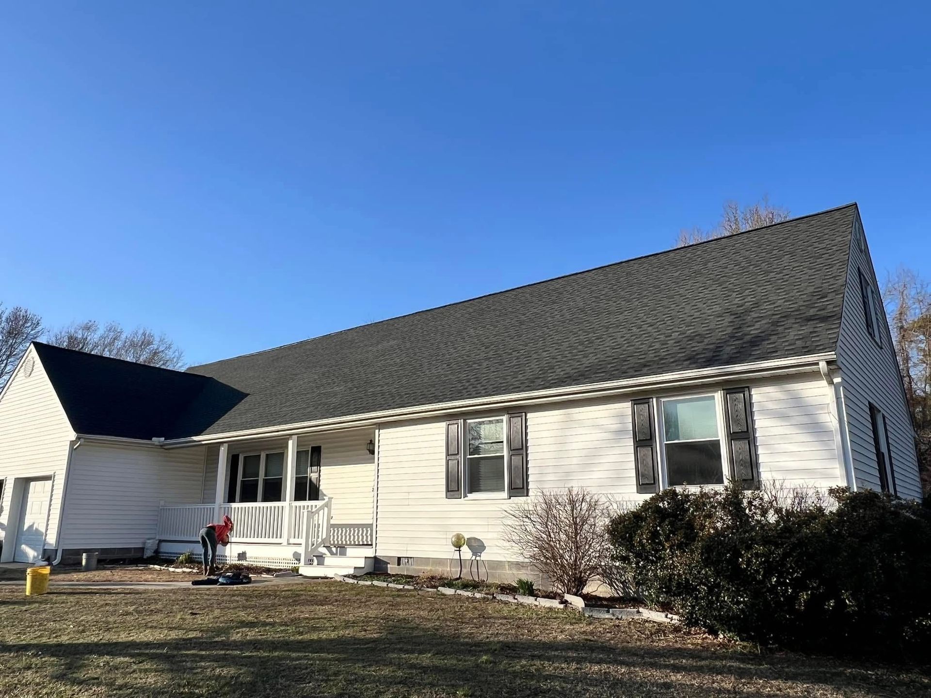 White single-story house with dark roof and front porch under a clear blue sky.