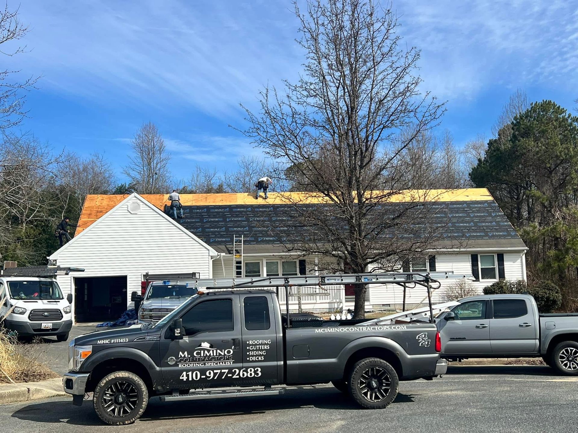 House with roof repair, pickup trucks parked in front under a blue sky.