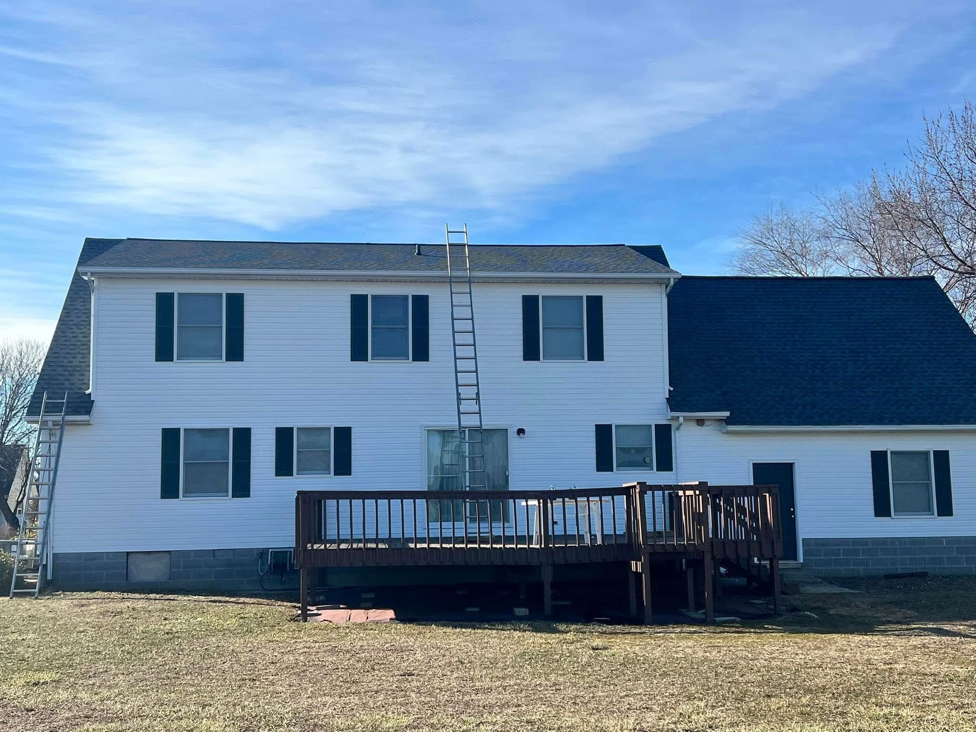 Two-story white house with dark shutters and a wooden deck under a blue sky