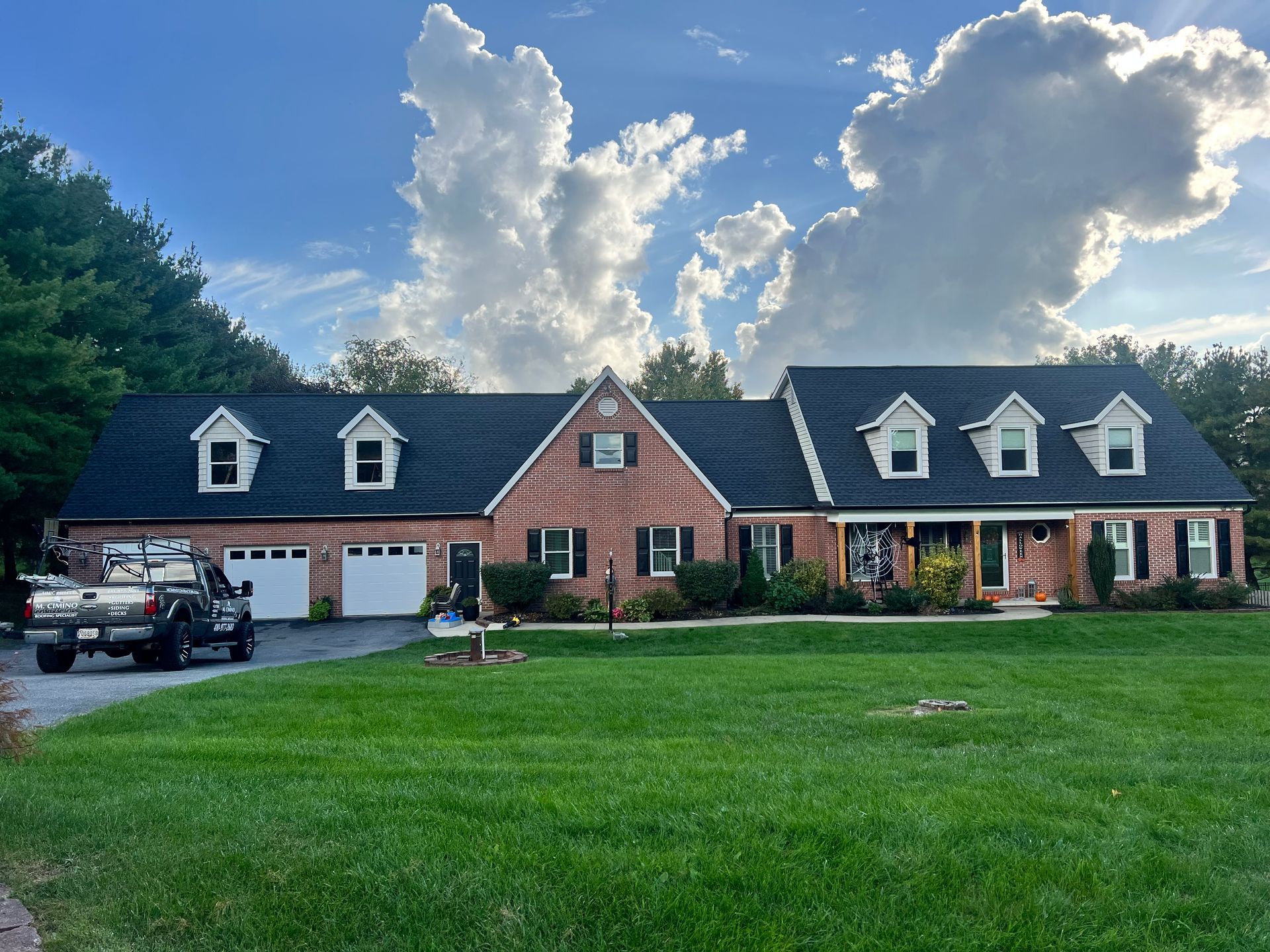 Large brick house with dark roof, garage, parked truck, and green lawn under a cloudy sky