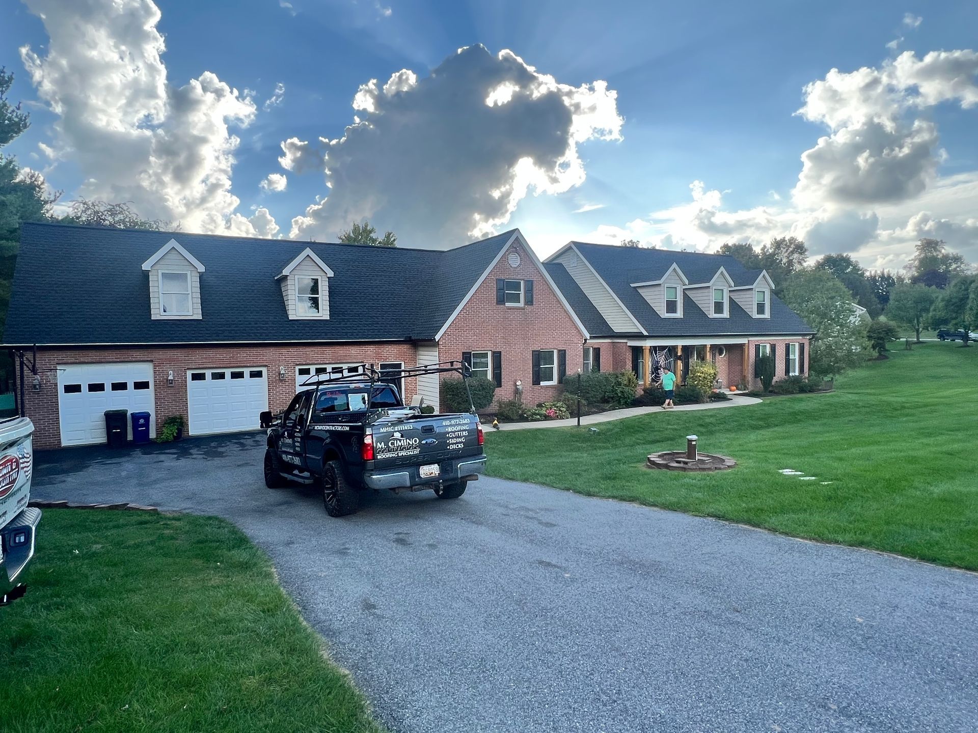 Brick suburban house with dark roof, gravel driveway, black pickup truck, and cloudy sky at sunset