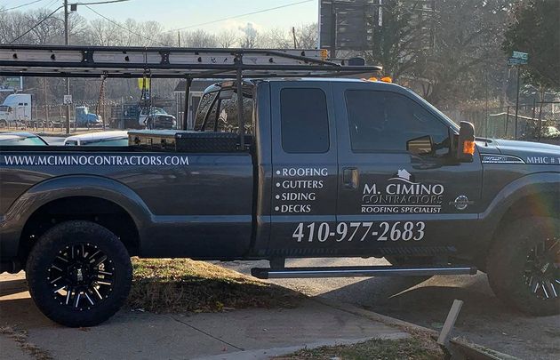 Black pickup truck with company lettering and phone number parked by a sidewalk