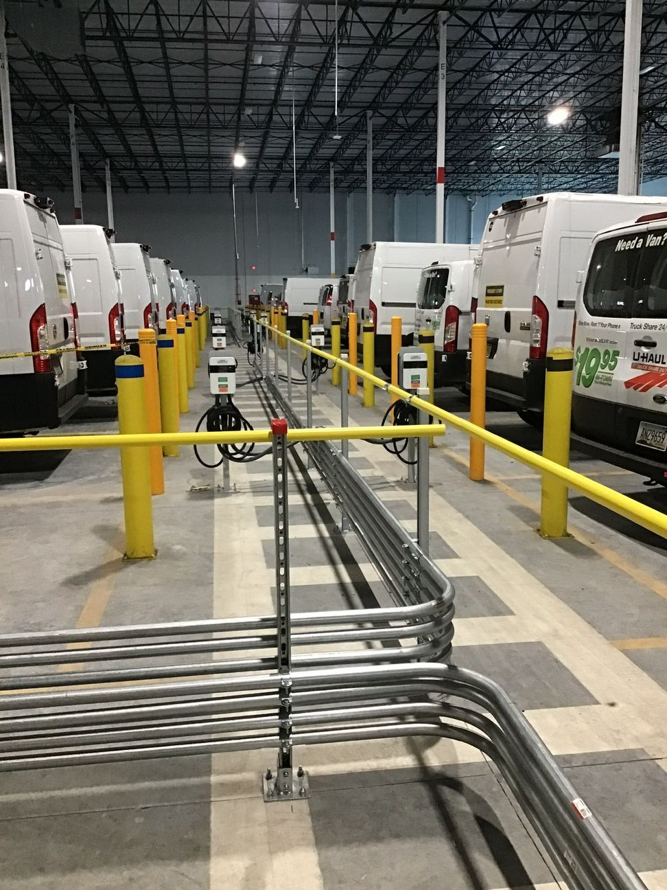 Warehouse aisle with white utility trucks, yellow safety rails, and overhead cable trays
