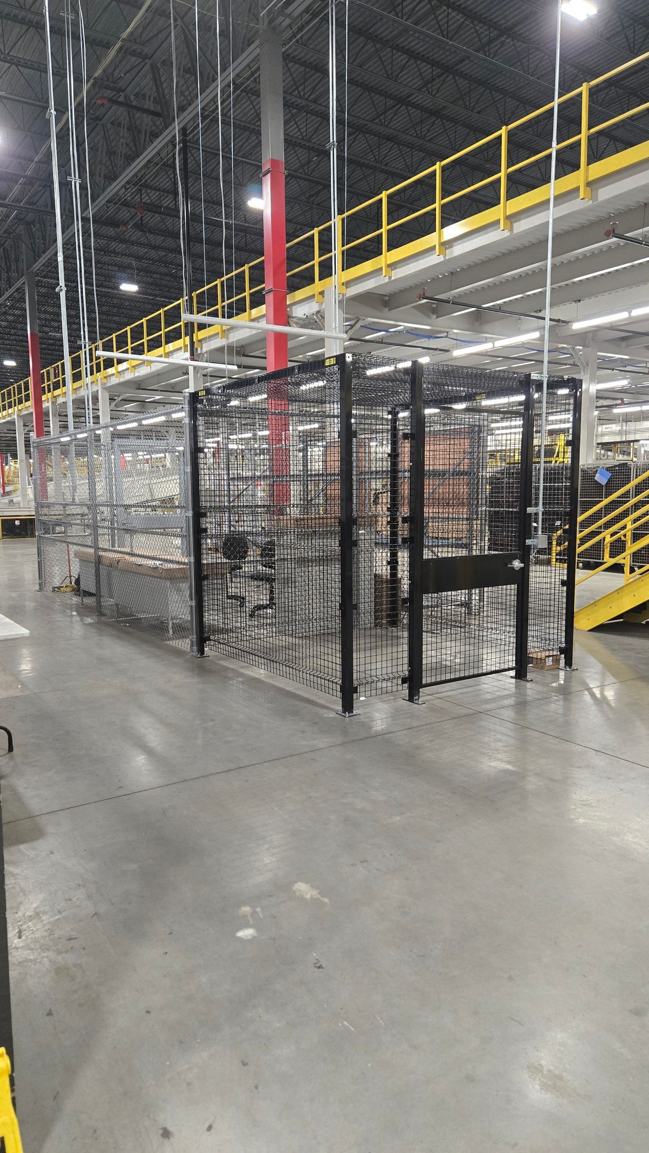 Industrial warehouse aisle with metal cages, yellow catwalk railing, and red safety post on a concrete floor