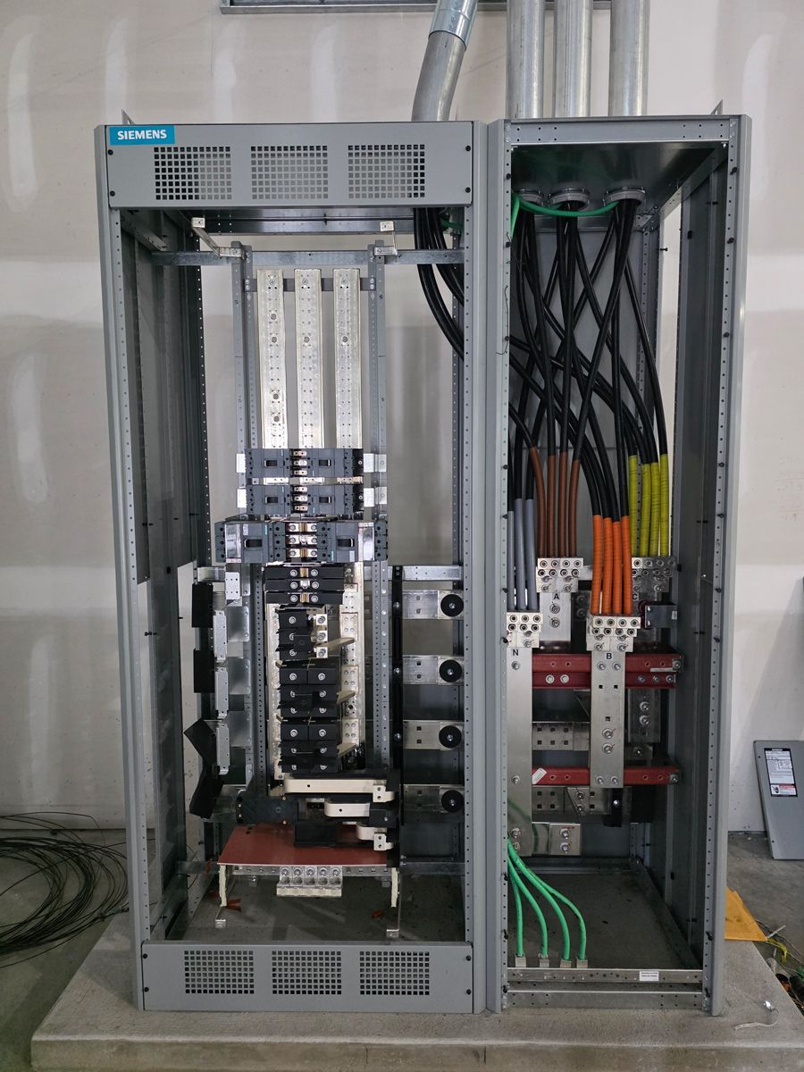 Open electrical control cabinet with wiring, breakers, and panels inside a metal enclosure
