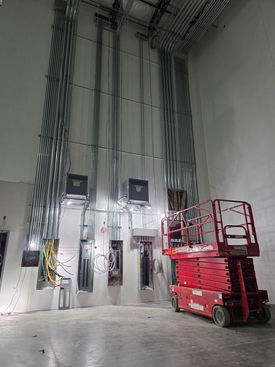 Industrial interior with tall cable runs on a concrete wall and a red scissor lift on the floor