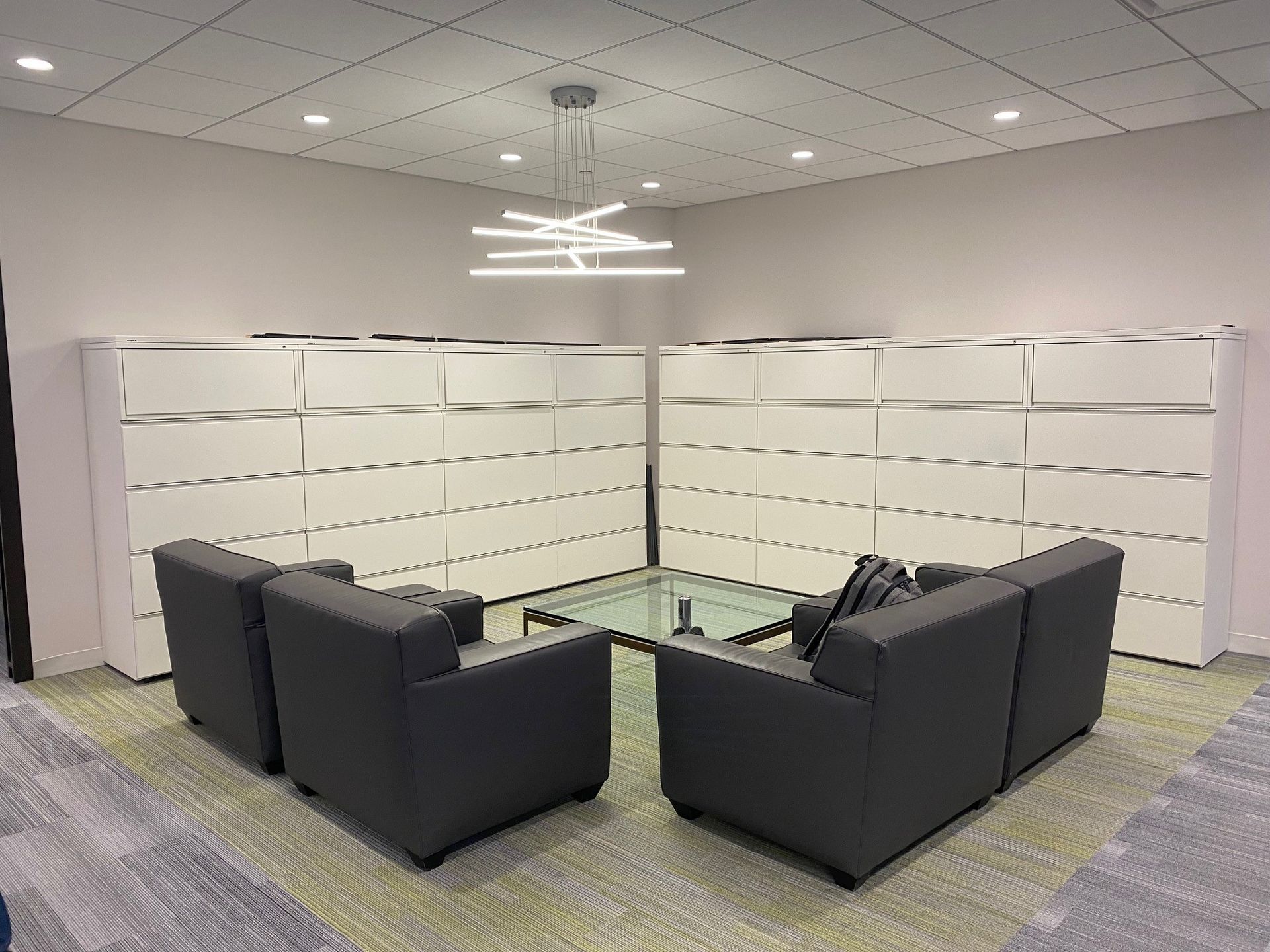 Modern office lounge with black sofas around a glass coffee table and white cubicle partitions