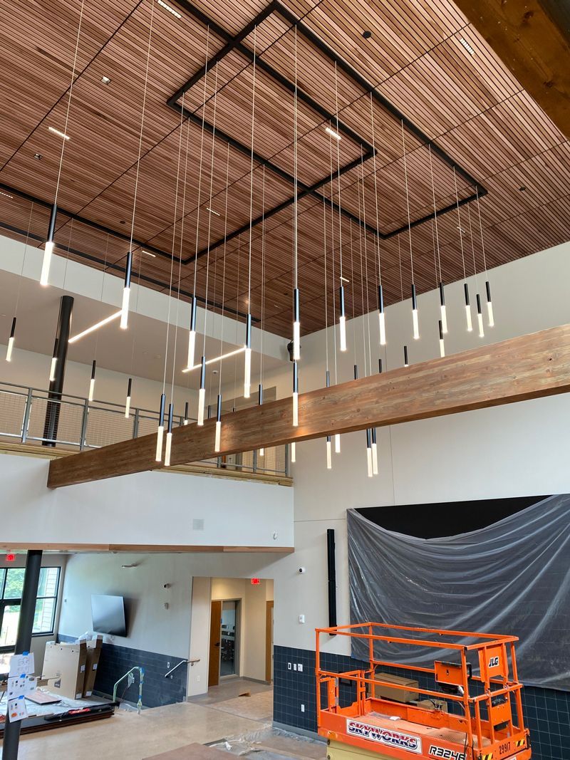 Interior under construction with tall wood ceiling, hanging pendant lights, and orange lift equipment