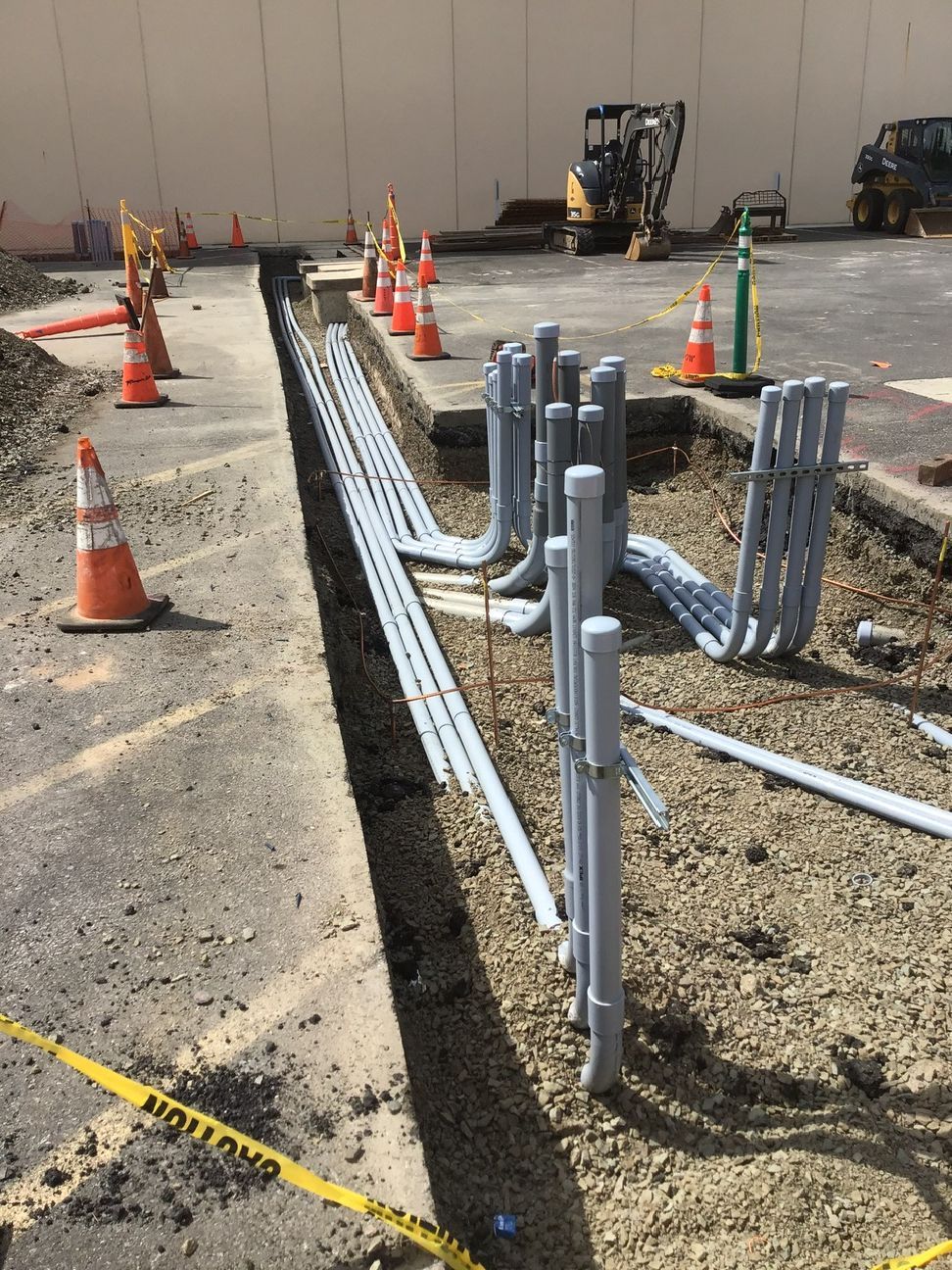 Construction trench with orange cones and exposed gray utility pipes on gravel.