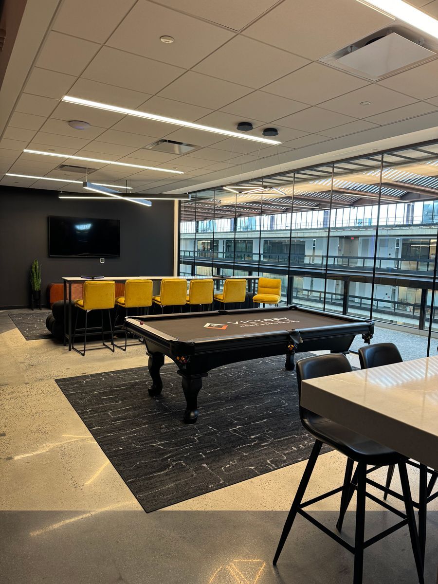 Modern lounge with pool table, yellow seating, TV, and large windows overlooking a city skyline