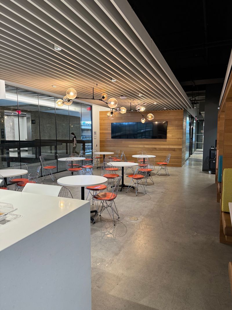Modern cafe seating area with white tables, orange stools, and a wood-paneled wall indoors