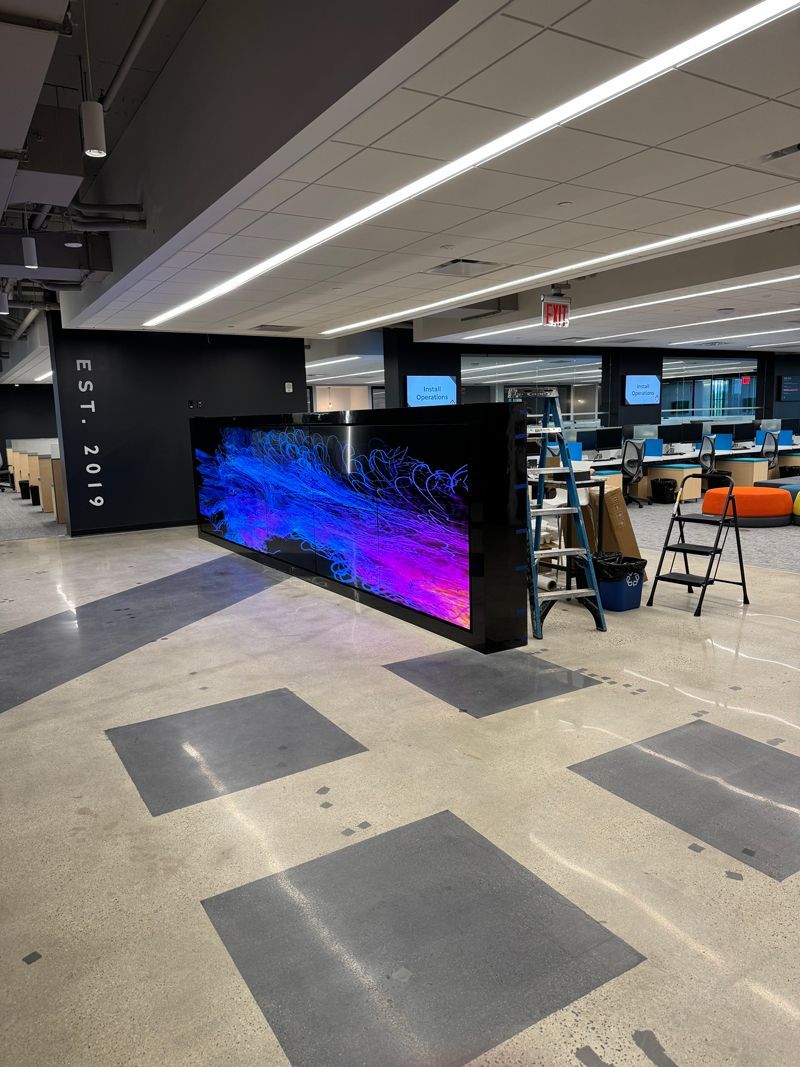 Modern office lounge with glowing blue-purple barrier, desks, monitors, and stools under bright ceiling lights