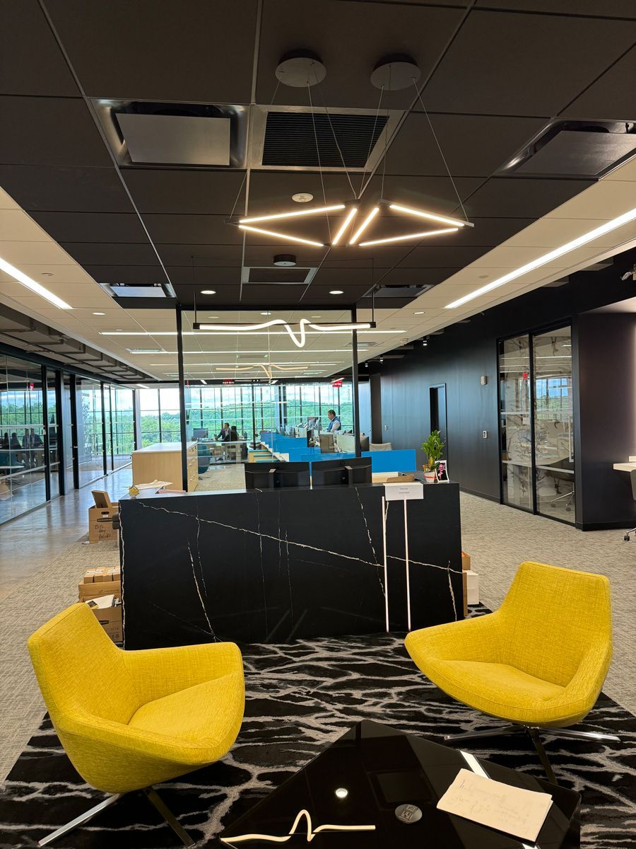 Modern office lounge with yellow chairs, black table, and glass-walled conference area
