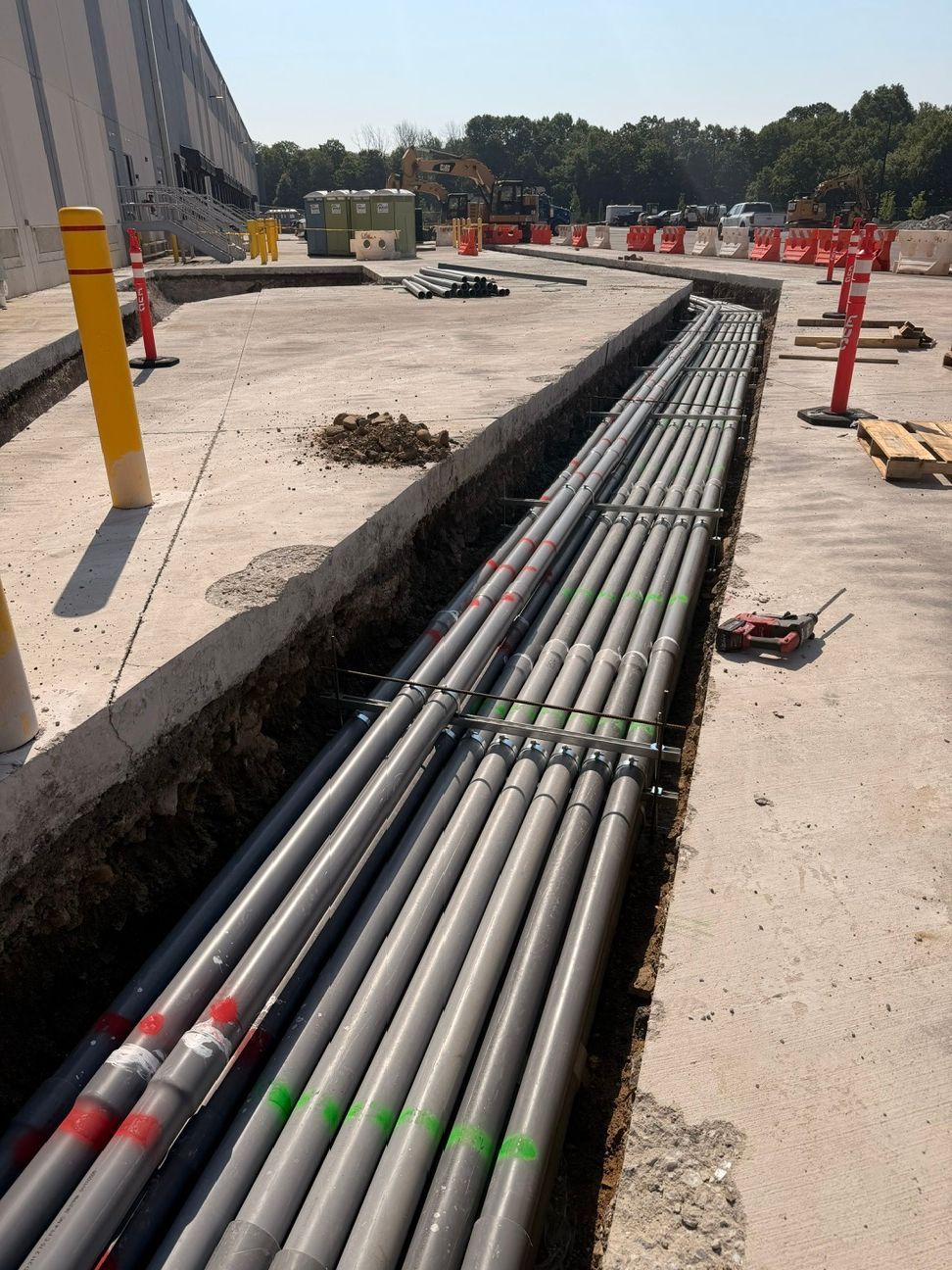 Underground cables laid in a trench beside a construction site road, with orange safety barriers nearby