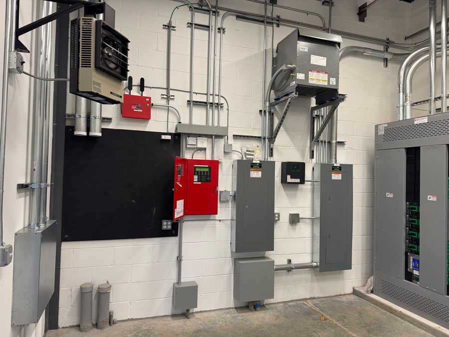 Electrical utility room with gray panels, red emergency box, and exposed conduit on a white brick wall