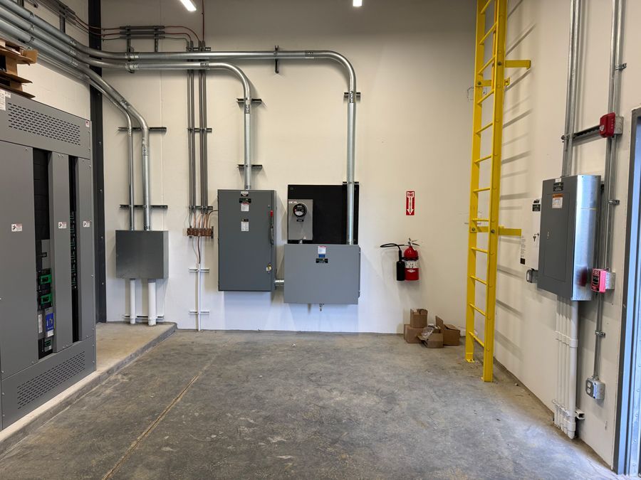 Industrial electrical room with gray control panels, wall conduits, and a yellow ladder against the wall