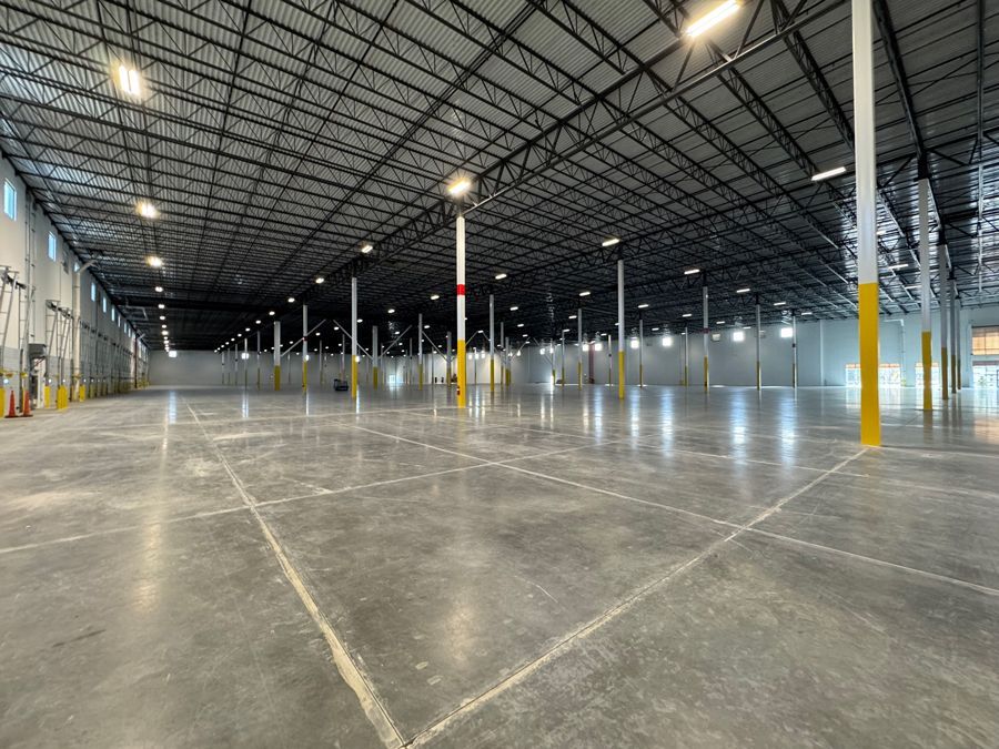 Empty warehouse interior with concrete floor, high metal ceiling, and bright overhead lights