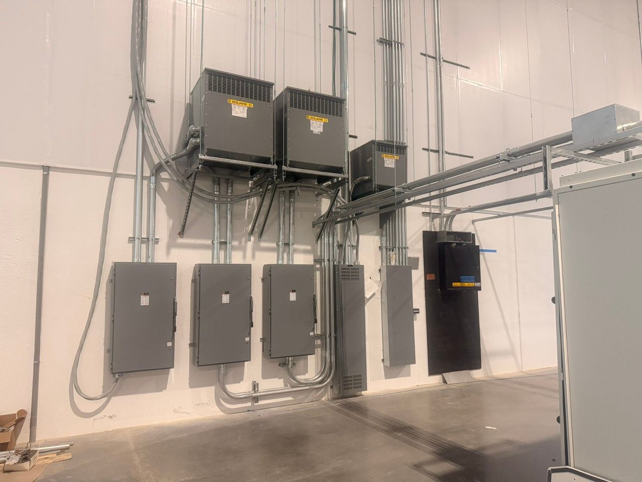 Electrical control panels and conduit mounted on a white industrial wall in a utility room.