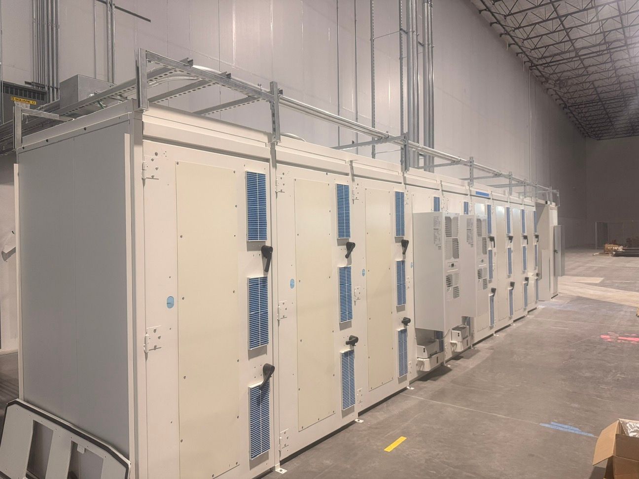 Row of beige electrical control cabinets with blue vents in an industrial room