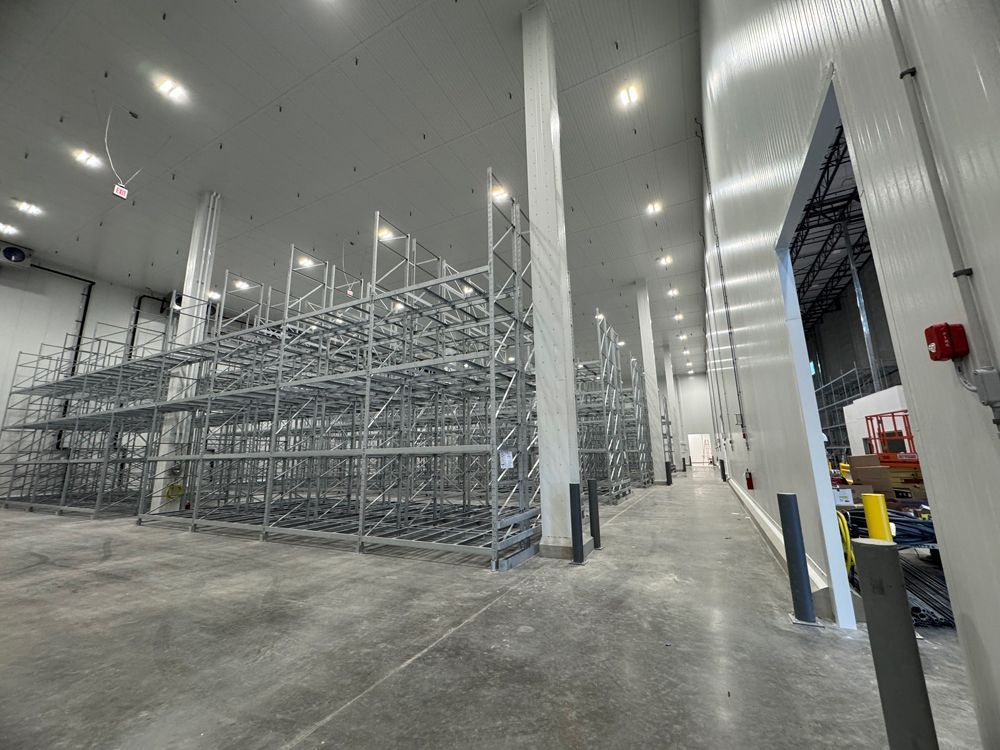 Large warehouse interior with metal storage racks and a concrete floor under bright overhead lights