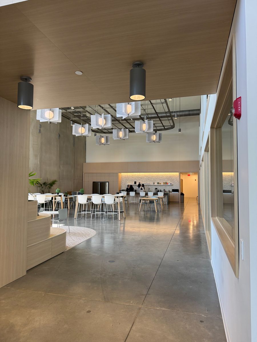Modern café interior with concrete floors, wooden ceiling, pendant lights, and white chairs around tables