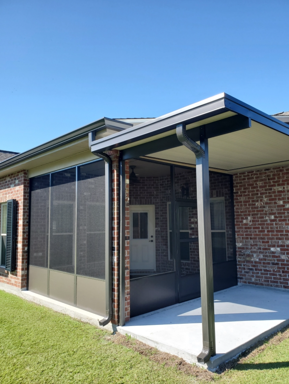 A screened in porch with a brick house in the background.