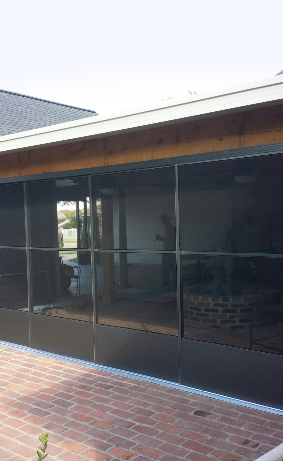 A screened in porch with a brick floor and a house in the background.