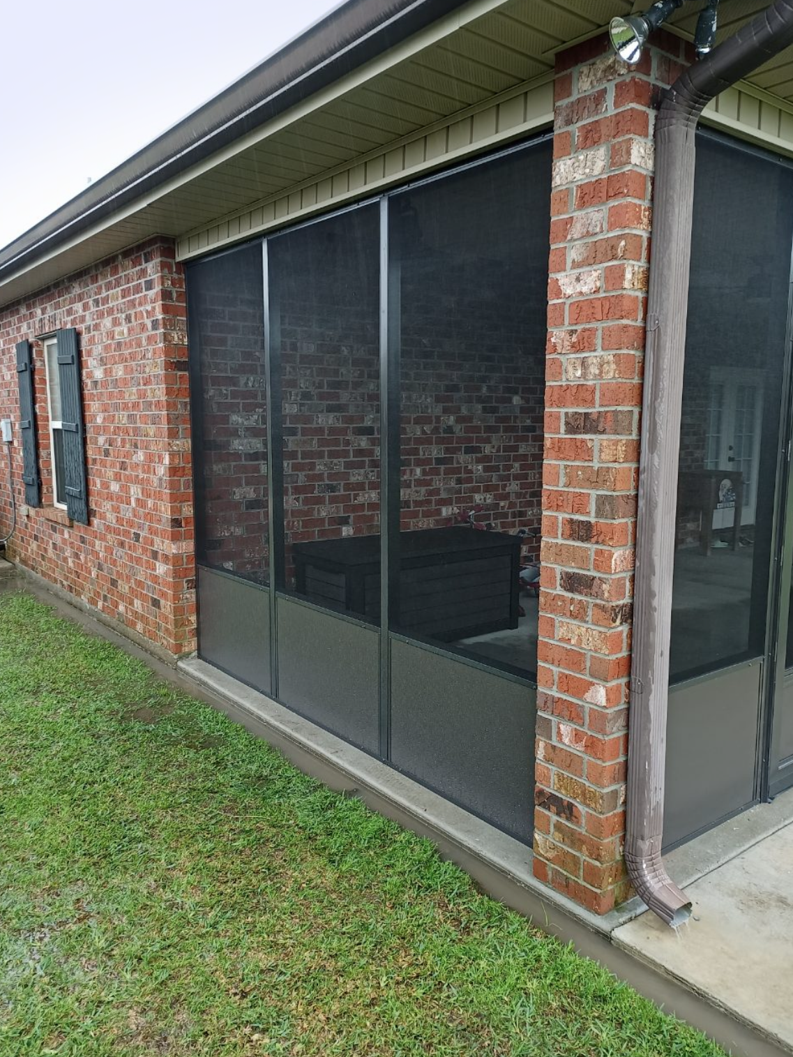 A screened in porch on the side of a brick house.