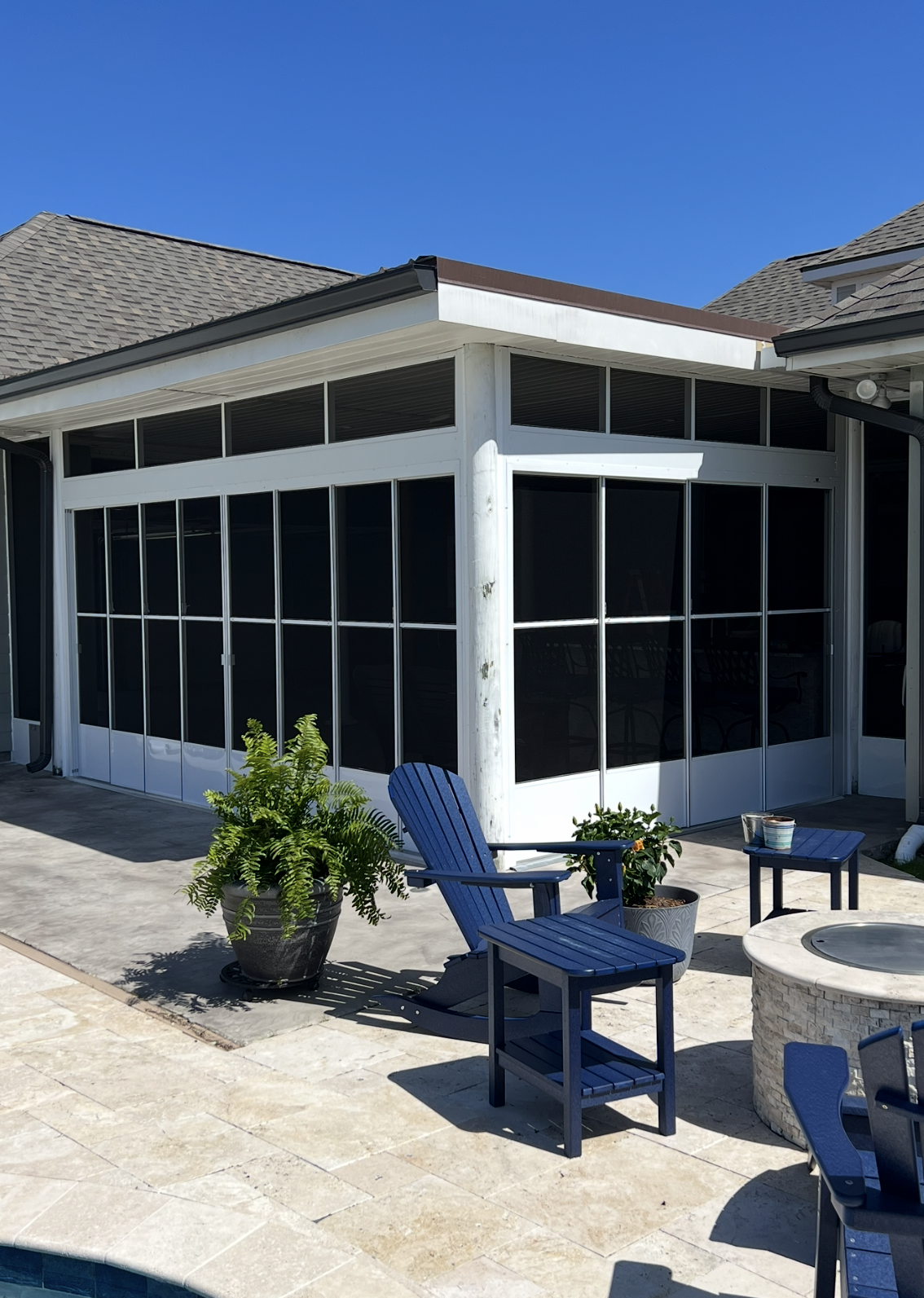 A screened in porch with chairs, tables, and a fire pit.