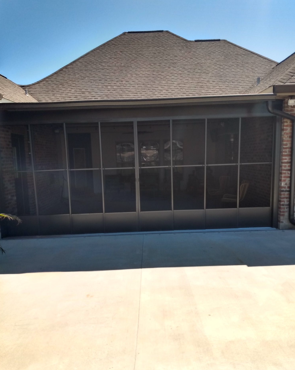 A screened in garage door with a brick house in the background.