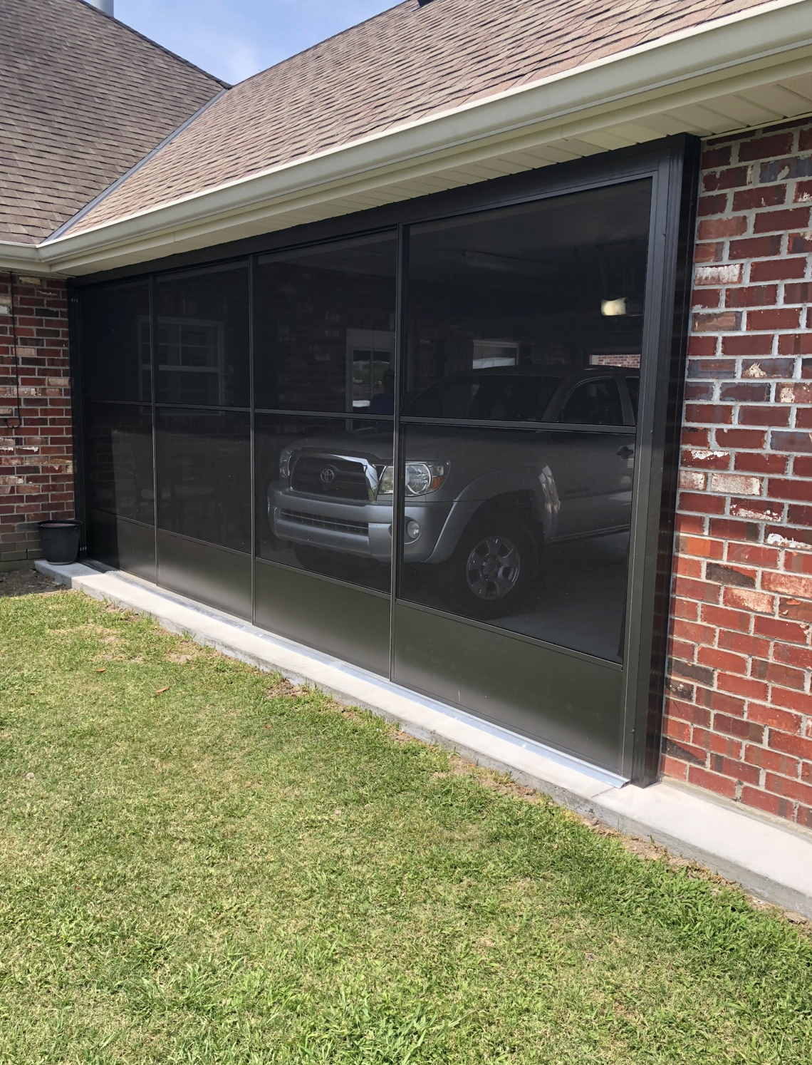 A car is parked in front of a brick house with a screen door.