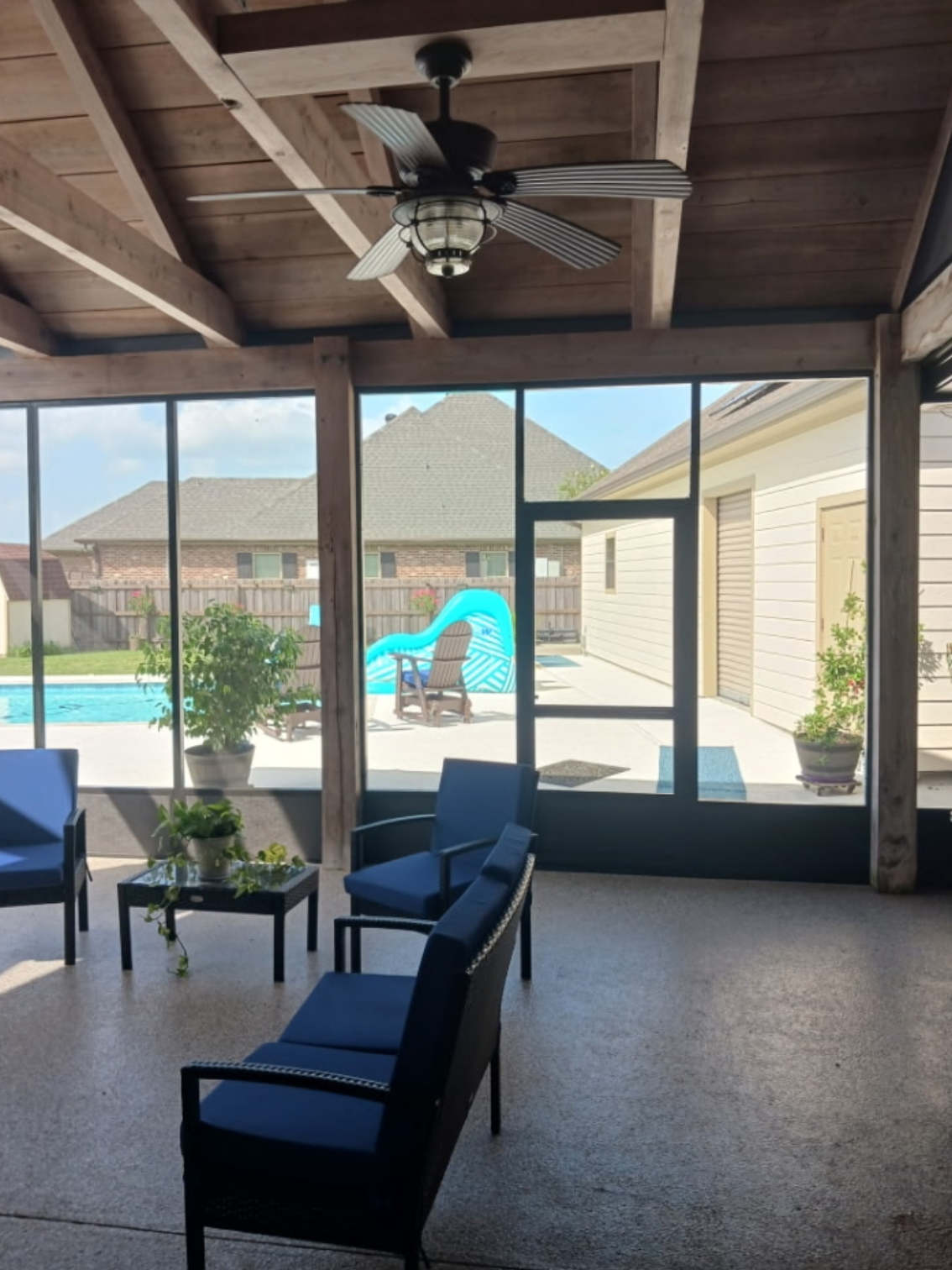 A screened in porch with chairs and a ceiling fan.