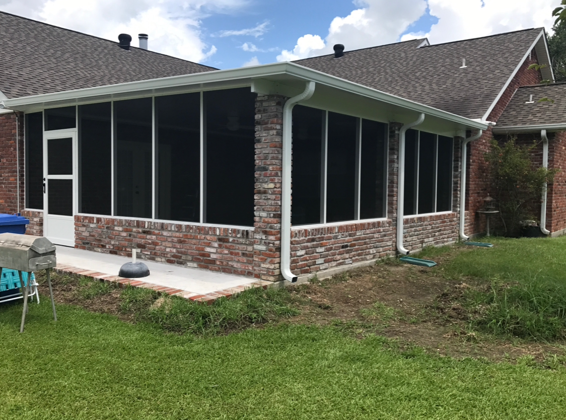 A screened in porch on the side of a brick house.