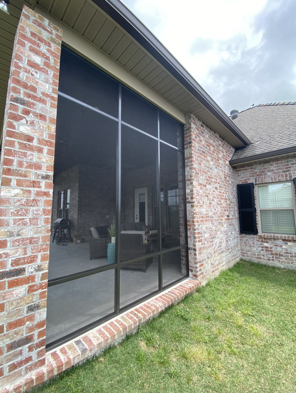A brick house with a screened in porch and a large window.