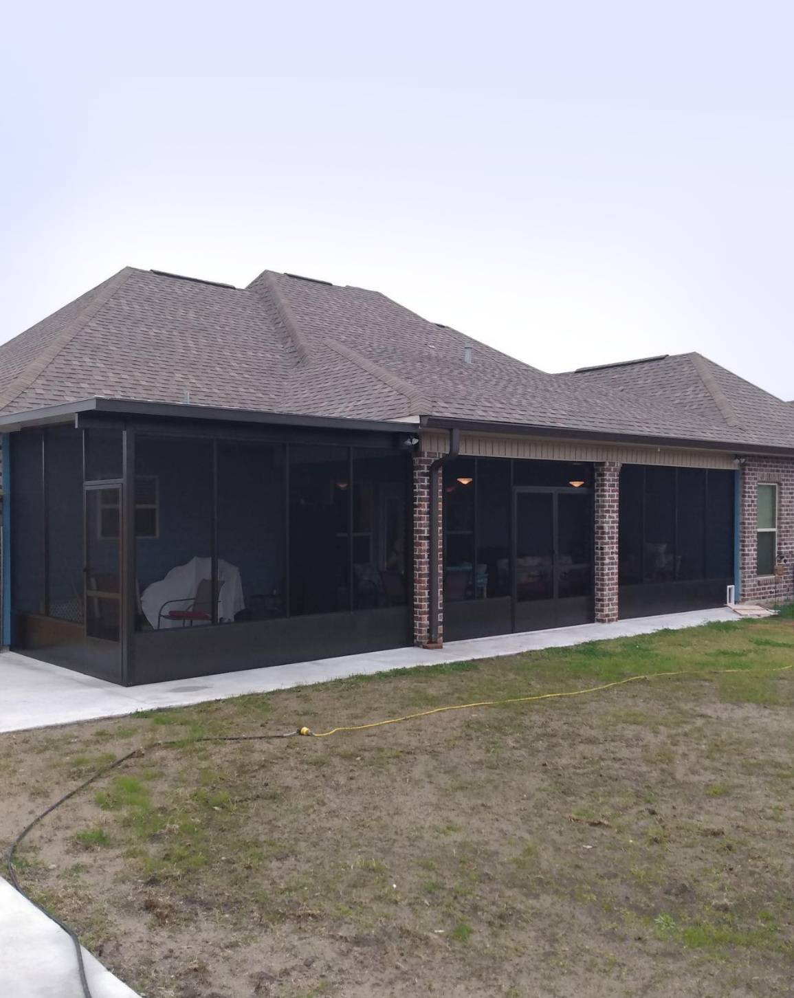 A house with a screened in porch and a large lawn in front of it.
