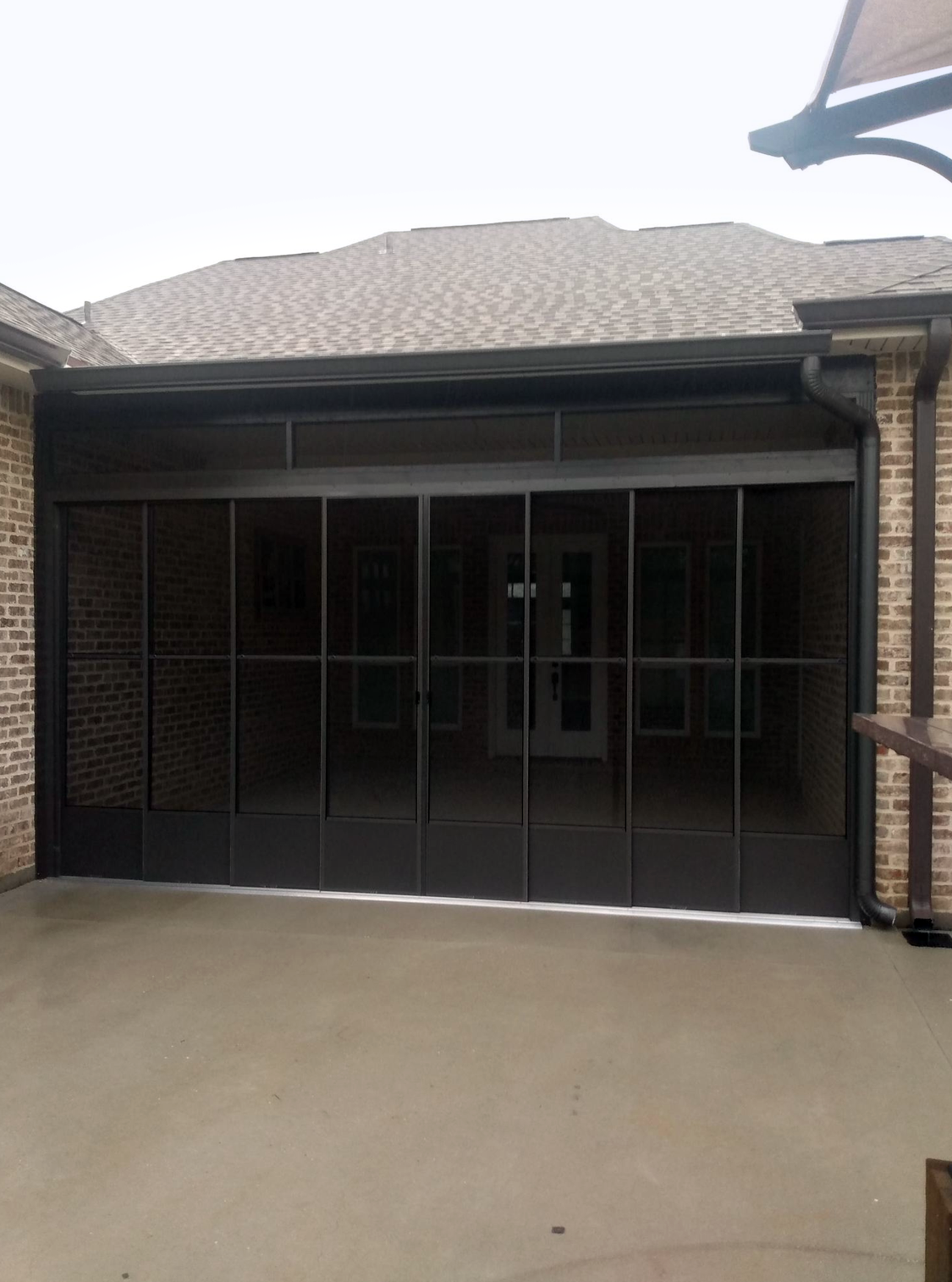 A screened in porch with a brick house in the background.
