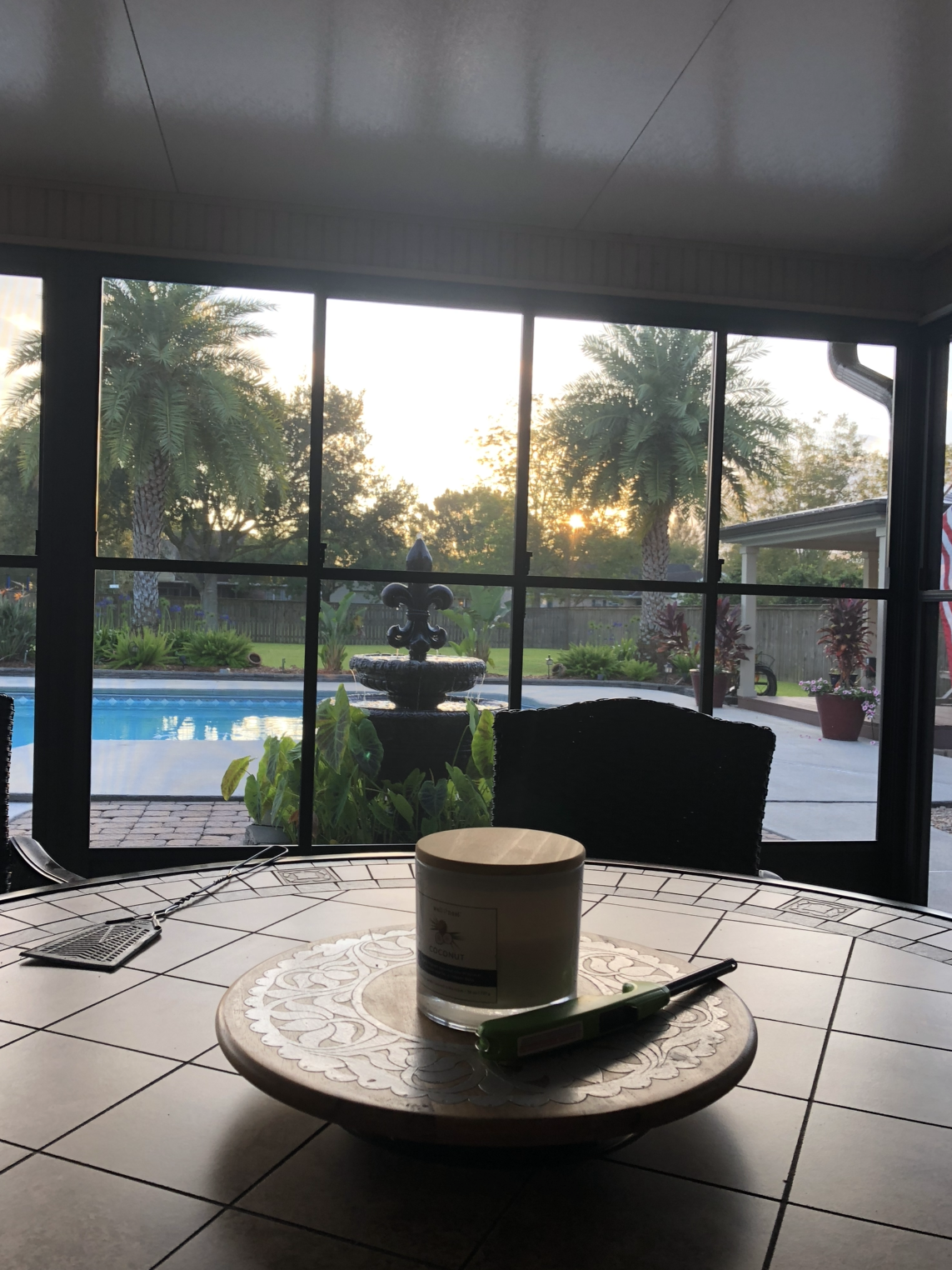 A candle sits on a table in front of a window overlooking a pool.