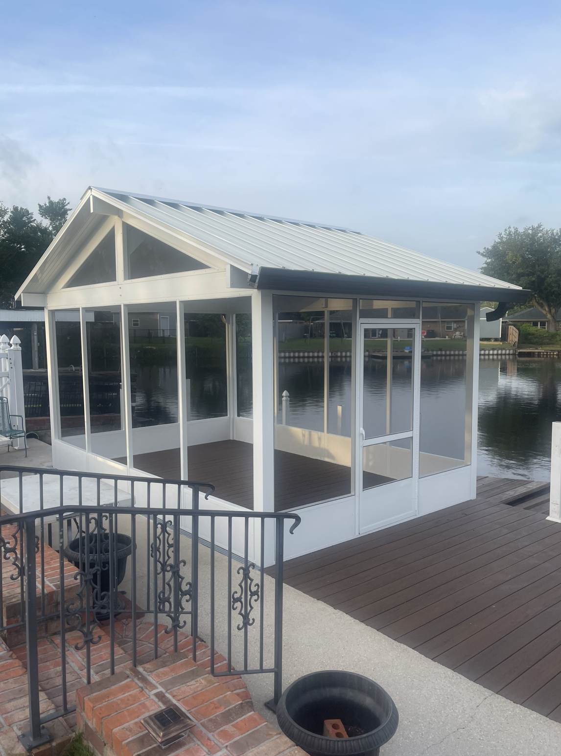 A white gazebo is sitting on top of a wooden deck next to a body of water.
