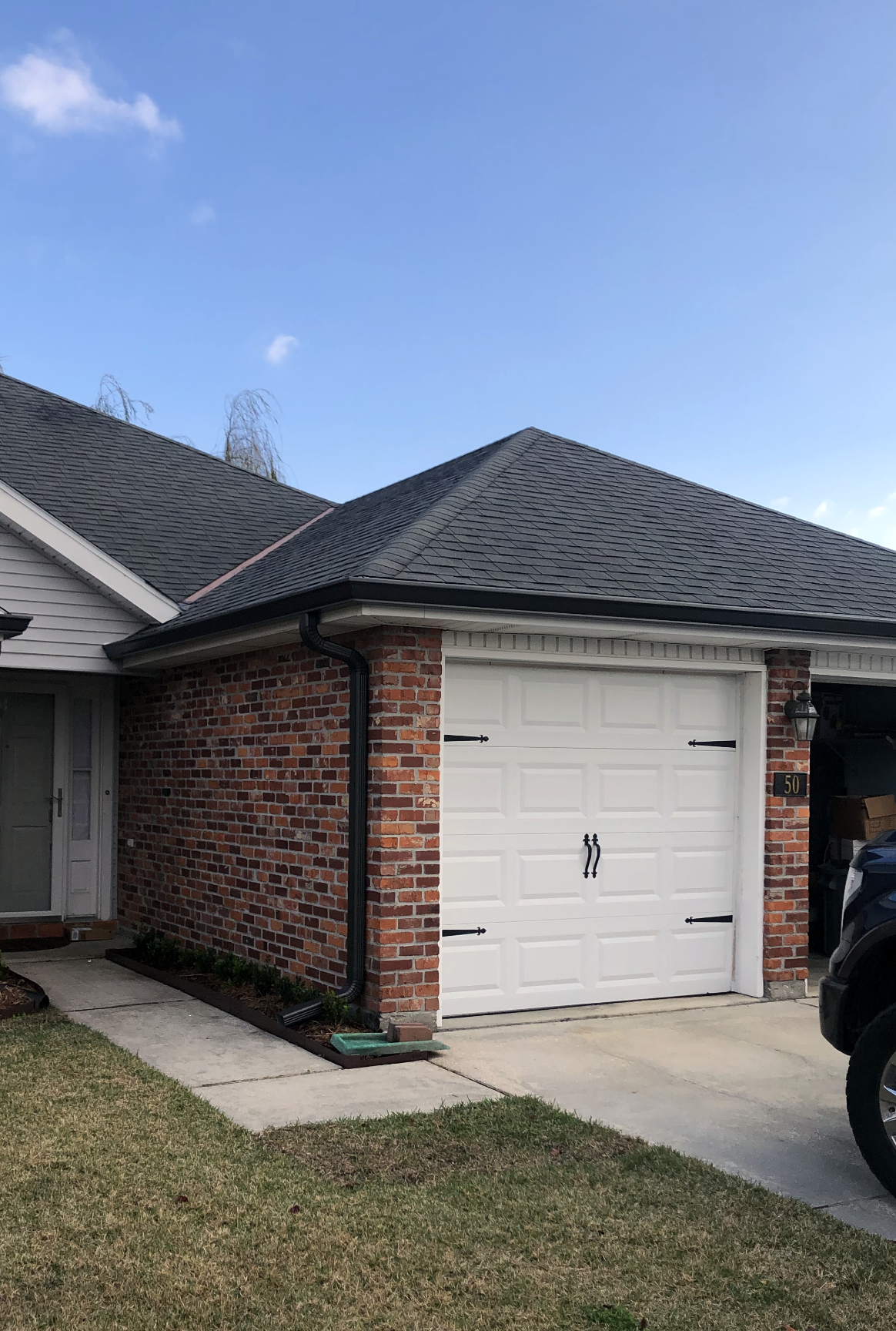 A car is parked in front of a brick house with a white garage door.