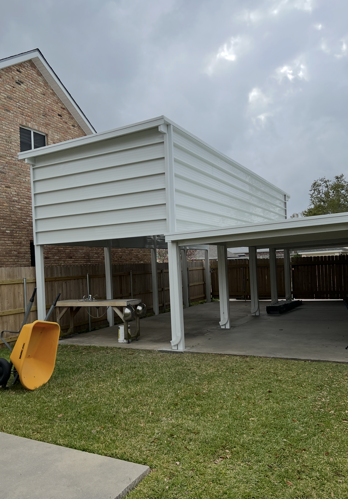 A white carport with a yellow wheelbarrow in front of it.