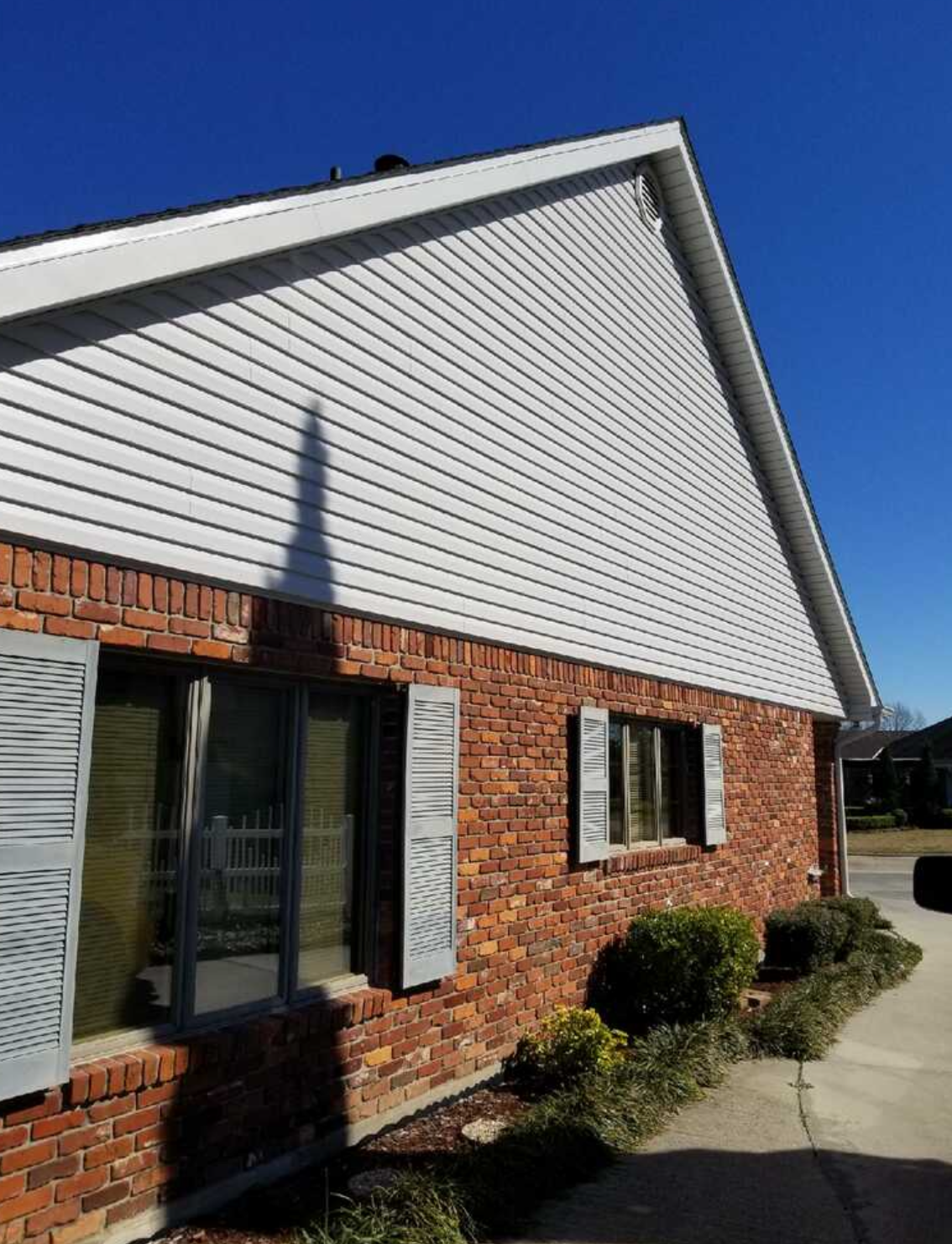 A brick house with white siding and shutters on a sunny day.