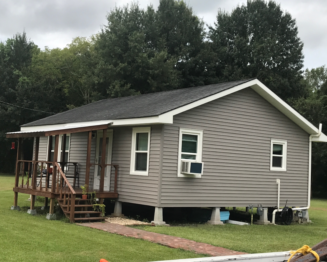 A small house with a porch and stairs is sitting in the middle of a grassy field.