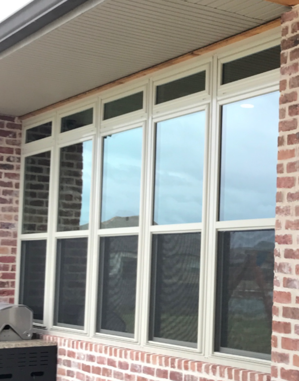 A white window with shutters on a brick wall.